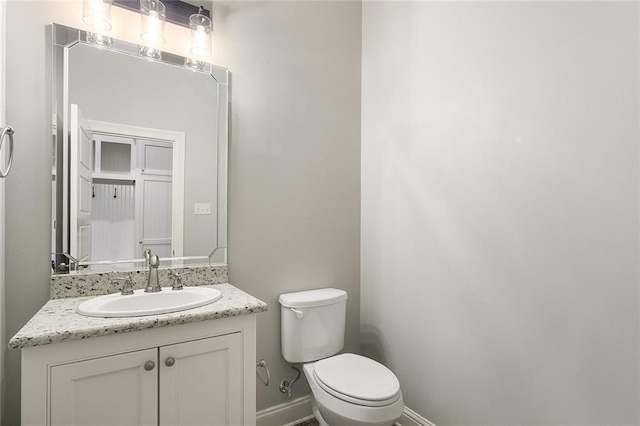 half bathroom with vanity, toilet, and baseboards
