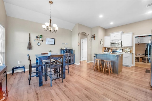 dining space with light wood-type flooring, lofted ceiling, baseboards, and an inviting chandelier