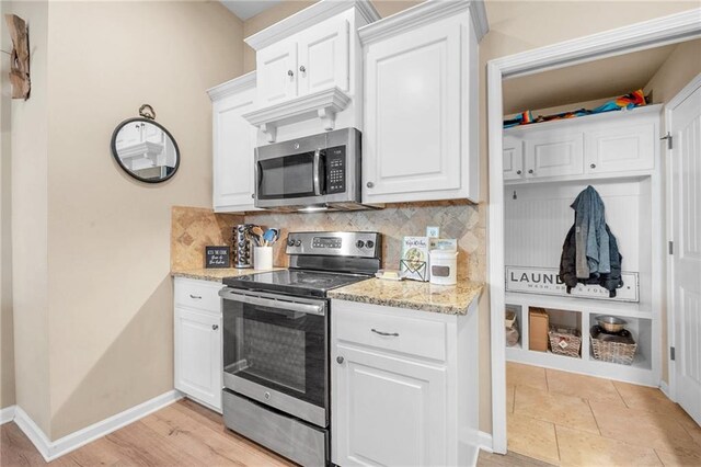 kitchen with tasteful backsplash, baseboards, white cabinetry, light stone counters, and appliances with stainless steel finishes