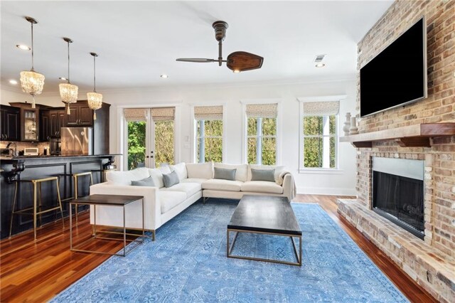 living area with visible vents, a ceiling fan, wood finished floors, a fireplace, and ornamental molding