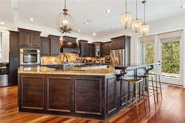 kitchen featuring custom exhaust hood, tasteful backsplash, an inviting chandelier, dark brown cabinetry, and freestanding refrigerator