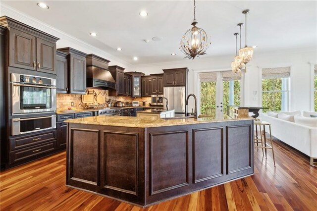 kitchen with a notable chandelier, dark brown cabinets, a sink, premium range hood, and ornamental molding