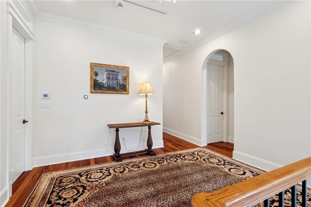 corridor featuring crown molding, wood finished floors, arched walkways, baseboards, and recessed lighting