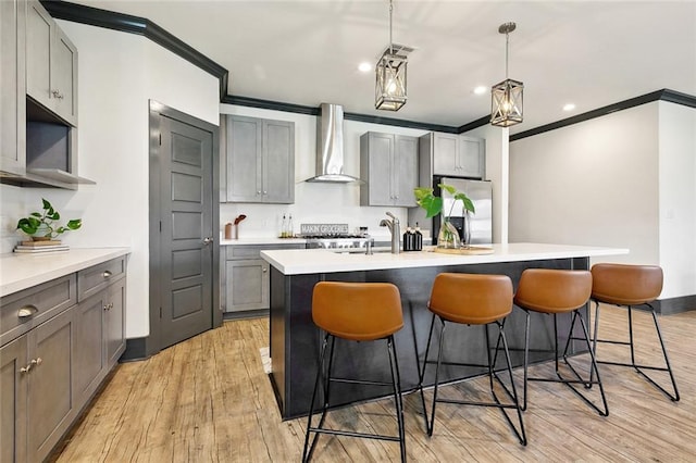 kitchen with wall chimney range hood, stainless steel fridge, gray cabinets, a kitchen bar, and ornamental molding