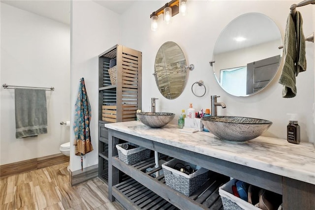 full bath with baseboards, a sink, double vanity, and toilet
