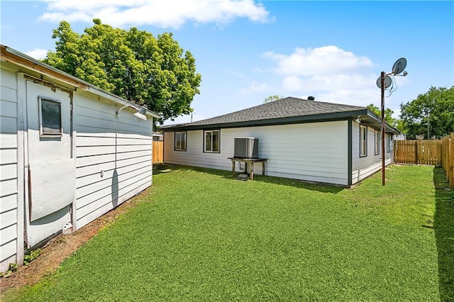 rear view of property featuring central air condition unit, a lawn, a fenced backyard, and roof with shingles