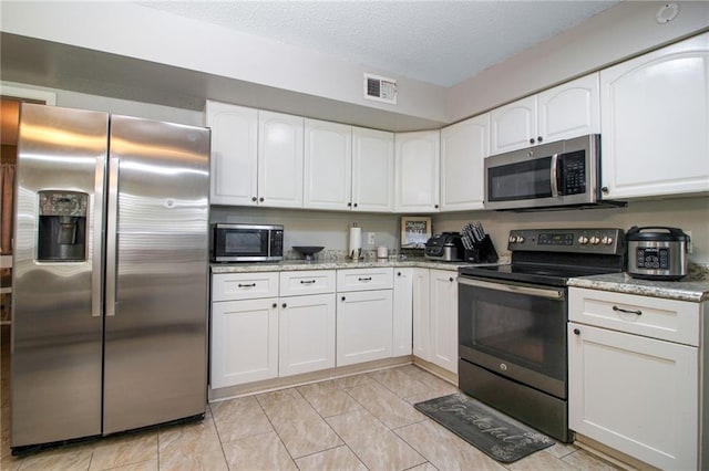2172 Carmel Valley Dr, La Place, LA 70068 - kitchen with a textured ceiling, white cabinets, appliances with stainless steel finishes, visible vents, and light stone countertops