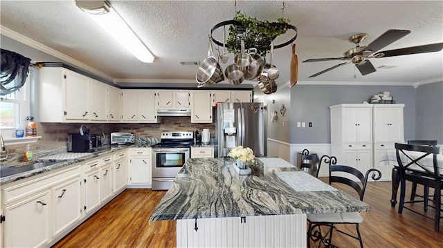 31763 Shelton Dr, Springfield, LA 70462 - kitchen with under cabinet range hood, stainless steel appliances, crown molding, a kitchen bar, and a textured ceiling
