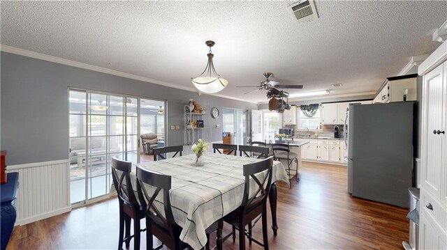 31763 Shelton Dr, Springfield, LA 70462 - dining space featuring a textured ceiling, dark wood-style flooring, visible vents, a ceiling fan, and ornamental molding