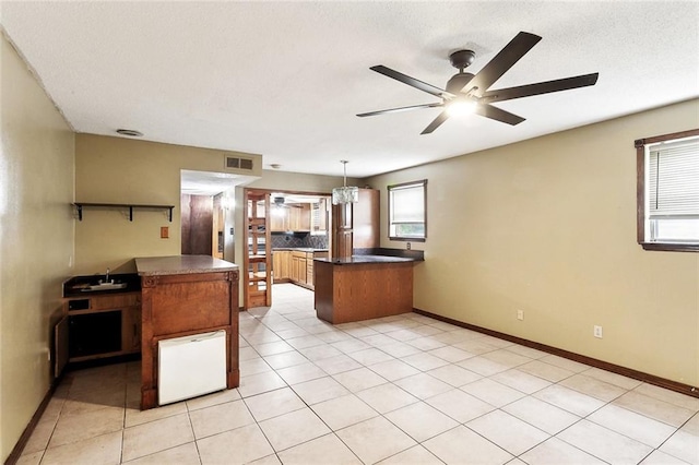 716 N Woodlawn Ave, Metairie, LA 70001 - kitchen with a peninsula, a ceiling fan, dark countertops, baseboards, and brown cabinets