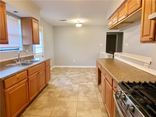 kitchen featuring brown cabinetry, visible vents, gas stove, a sink, and light tile patterned flooring