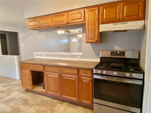 kitchen featuring stainless steel range with gas stovetop, light tile patterned flooring, under cabinet range hood, and brown cabinetry