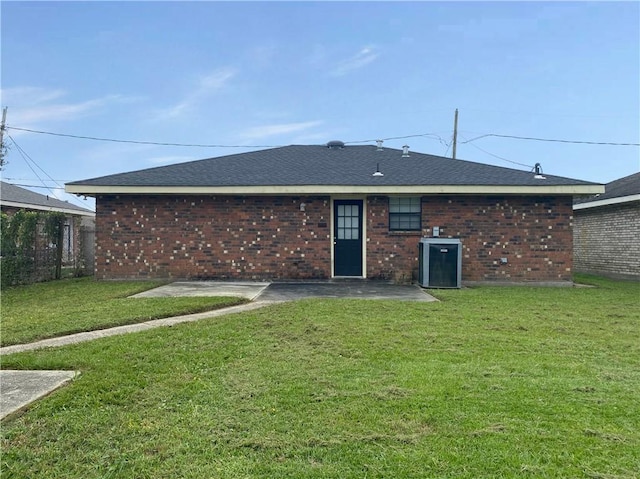 back of property with cooling unit, roof with shingles, brick siding, a patio area, and a lawn