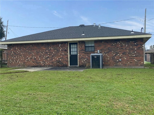 rear view of house featuring a lawn, a shingled roof, central air condition unit, and brick siding