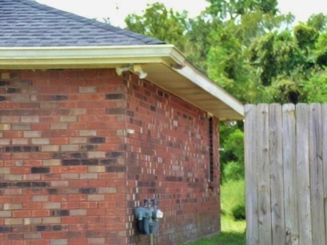 view of home's exterior with brick siding, fence, and a shingled roof