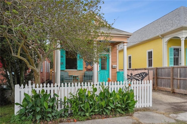 shotgun-style home with a porch, a shingled roof, and a fenced front yard
