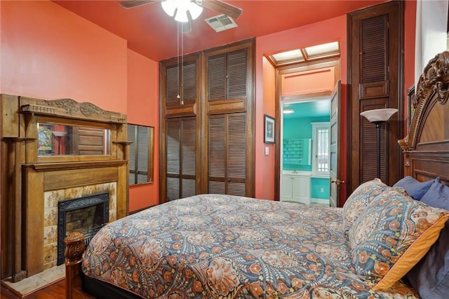 bedroom with ensuite bath, a premium fireplace, visible vents, and a ceiling fan