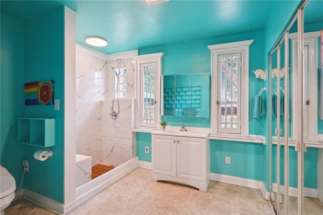 bathroom with baseboards, a marble finish shower, vanity, and a healthy amount of sunlight