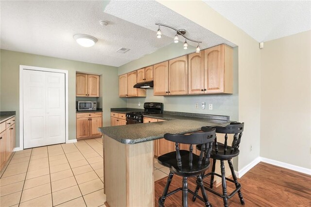 4740 W Esplanade Ave, Metairie, LA 70006 - kitchen with light brown cabinetry, under cabinet range hood, black range with gas stovetop, stainless steel microwave, and a peninsula