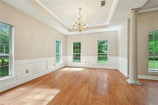 4761 Sharp Rd, Mandeville, LA 70471 - empty room featuring ornate columns, a chandelier, a tray ceiling, light wood-style flooring, and wainscoting