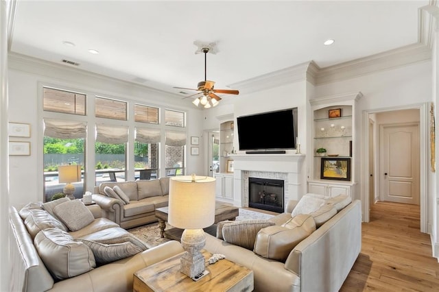 living room featuring ornamental molding, light wood finished floors, a ceiling fan, and a fireplace