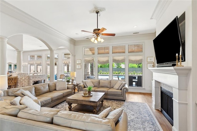 living room featuring a fireplace, ornamental molding, ornate columns, and ceiling fan