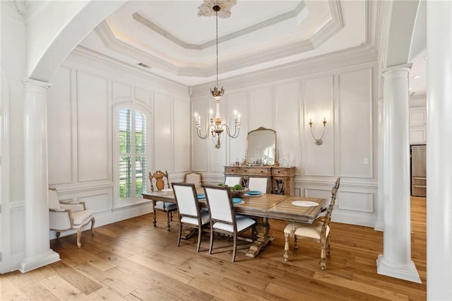 dining area featuring ornamental molding, light wood finished floors, decorative columns, and a decorative wall