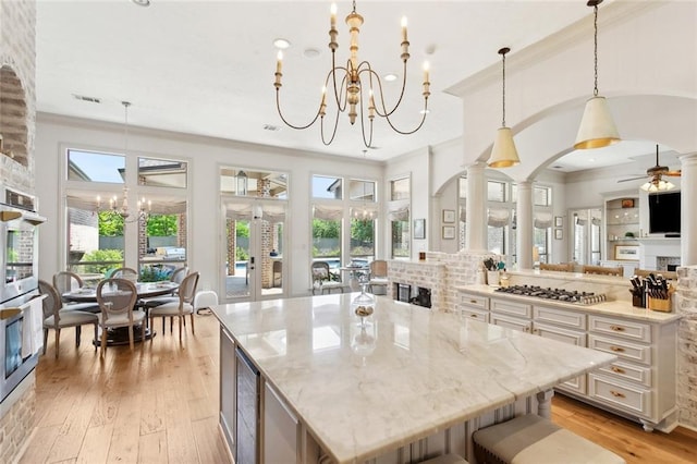kitchen with light stone countertops, wine cooler, decorative columns, light wood-type flooring, and ornamental molding