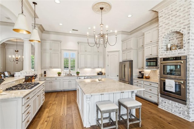 kitchen featuring light stone counters, a sink, appliances with stainless steel finishes, a chandelier, and a kitchen island