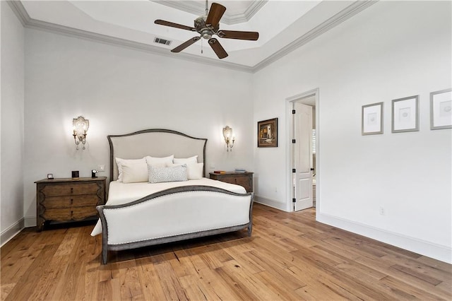bedroom featuring visible vents, a raised ceiling, crown molding, and light wood-style flooring
