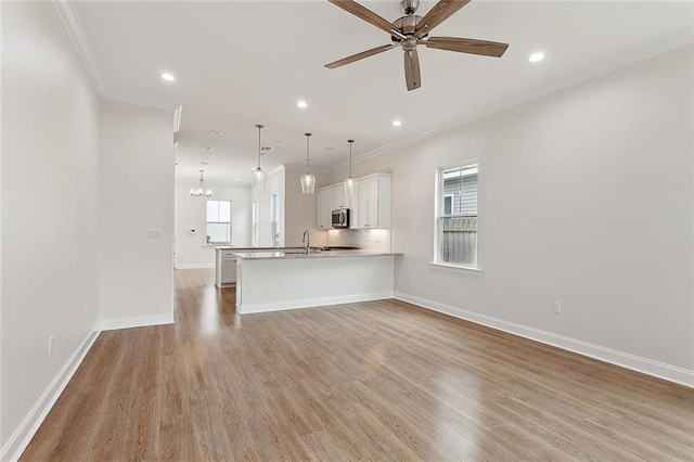 unfurnished living room featuring crown molding, recessed lighting, light wood-style flooring, and ceiling fan with notable chandelier
