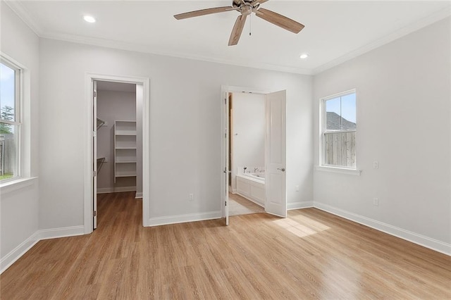 unfurnished bedroom featuring a walk in closet, baseboards, light wood-style floors, and crown molding