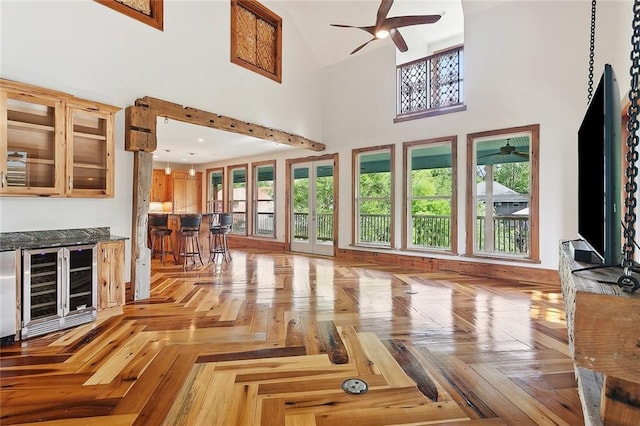unfurnished living room with a dry bar, wine cooler, high vaulted ceiling, and a ceiling fan
