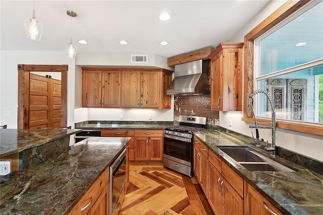 kitchen with stainless steel appliances, a sink, visible vents, wall chimney range hood, and decorative light fixtures