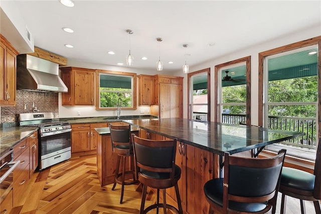 kitchen featuring stainless steel range with gas cooktop, recessed lighting, backsplash, wall chimney range hood, and a kitchen island