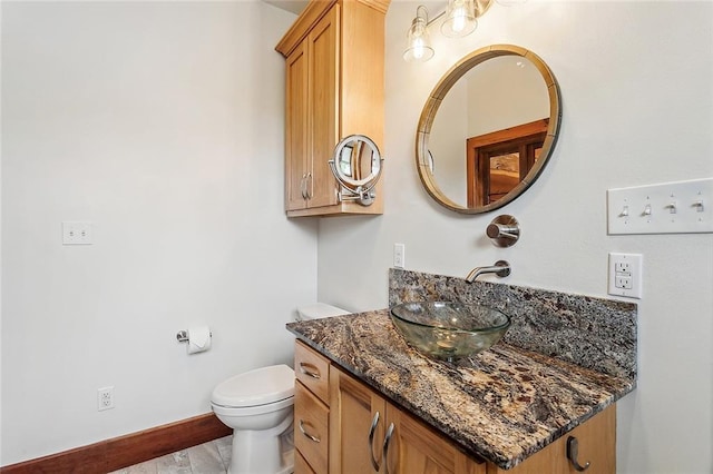 half bathroom featuring baseboards, toilet, and vanity