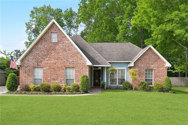 view of front of house featuring fence, a shingled roof, a front lawn, and brick siding