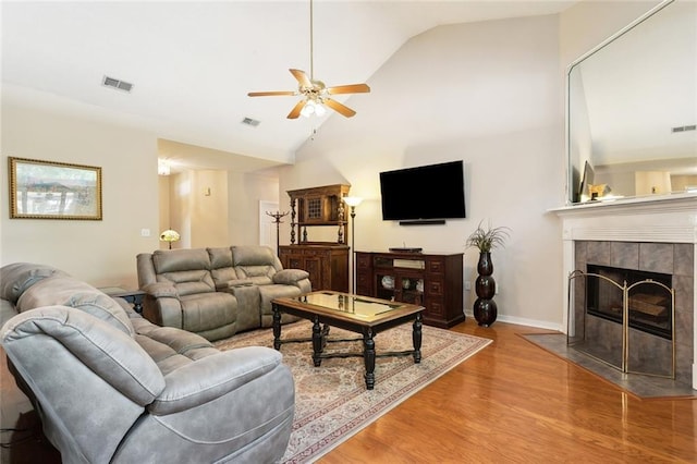 living area featuring vaulted ceiling, visible vents, a ceiling fan, wood finished floors, and a tile fireplace