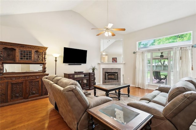 living area featuring a tile fireplace, vaulted ceiling, a ceiling fan, and light wood-style floors