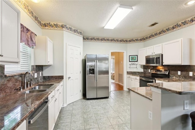 kitchen featuring a textured ceiling, appliances with stainless steel finishes, dark stone countertops, and a sink
