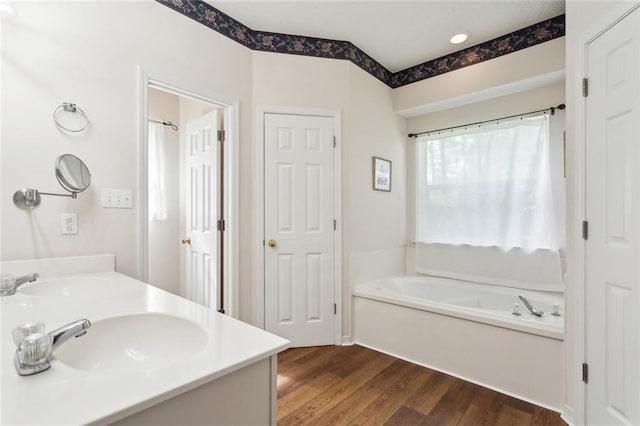 bathroom featuring a garden tub, wood finished floors, a sink, and double vanity