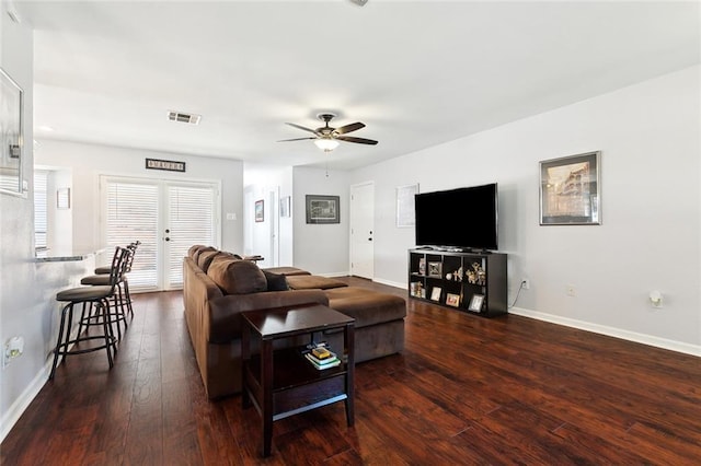 living room with dark wood-style flooring, visible vents, a ceiling fan, and baseboards