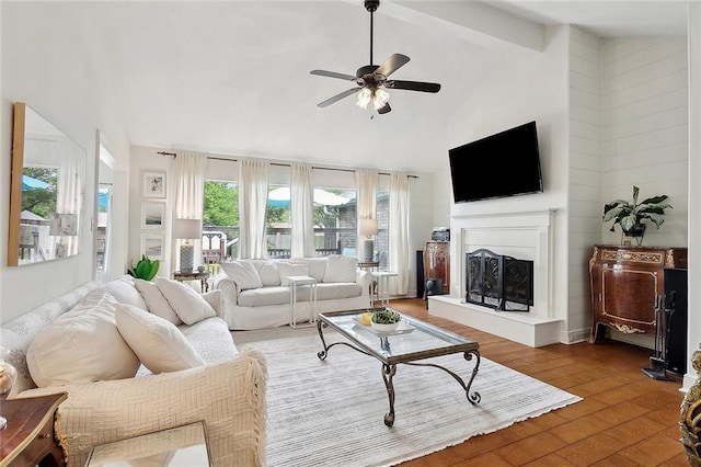 living room with high vaulted ceiling, a ceiling fan, a fireplace with raised hearth, beamed ceiling, and wood-type flooring