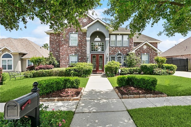 traditional home featuring stucco siding, a front yard, french doors, and brick siding