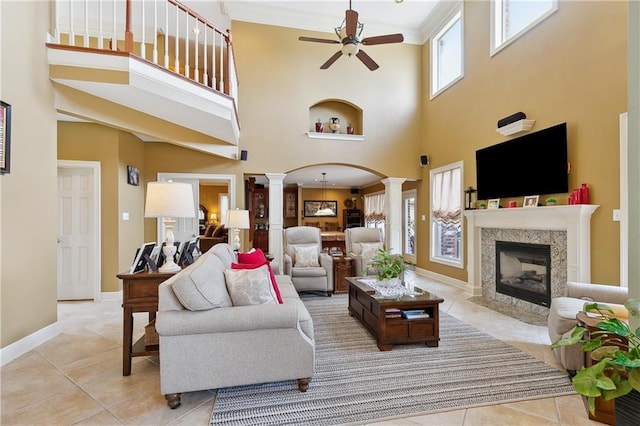 living room featuring a tiled fireplace, tile patterned floors, ceiling fan, ornate columns, and a high ceiling