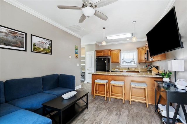 living room featuring crown molding, light wood finished floors, a ceiling fan, and visible vents