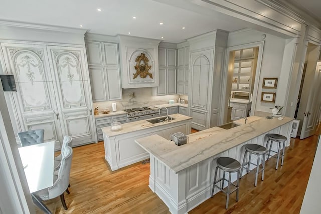 1711 Palmer Ave, New Orleans, LA 70118 - kitchen with a kitchen island with sink, a sink, a breakfast bar, crown molding, and light wood-style flooring