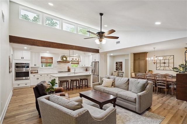living area featuring light wood-style floors, high vaulted ceiling, a wealth of natural light, and ceiling fan with notable chandelier
