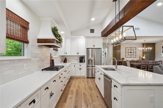 kitchen with appliances with stainless steel finishes, vaulted ceiling, a sink, visible vents, and premium range hood