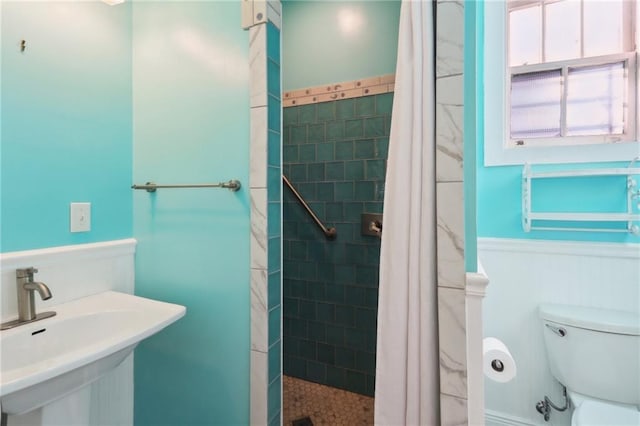 full bath featuring wainscoting, tiled shower, toilet, and a sink